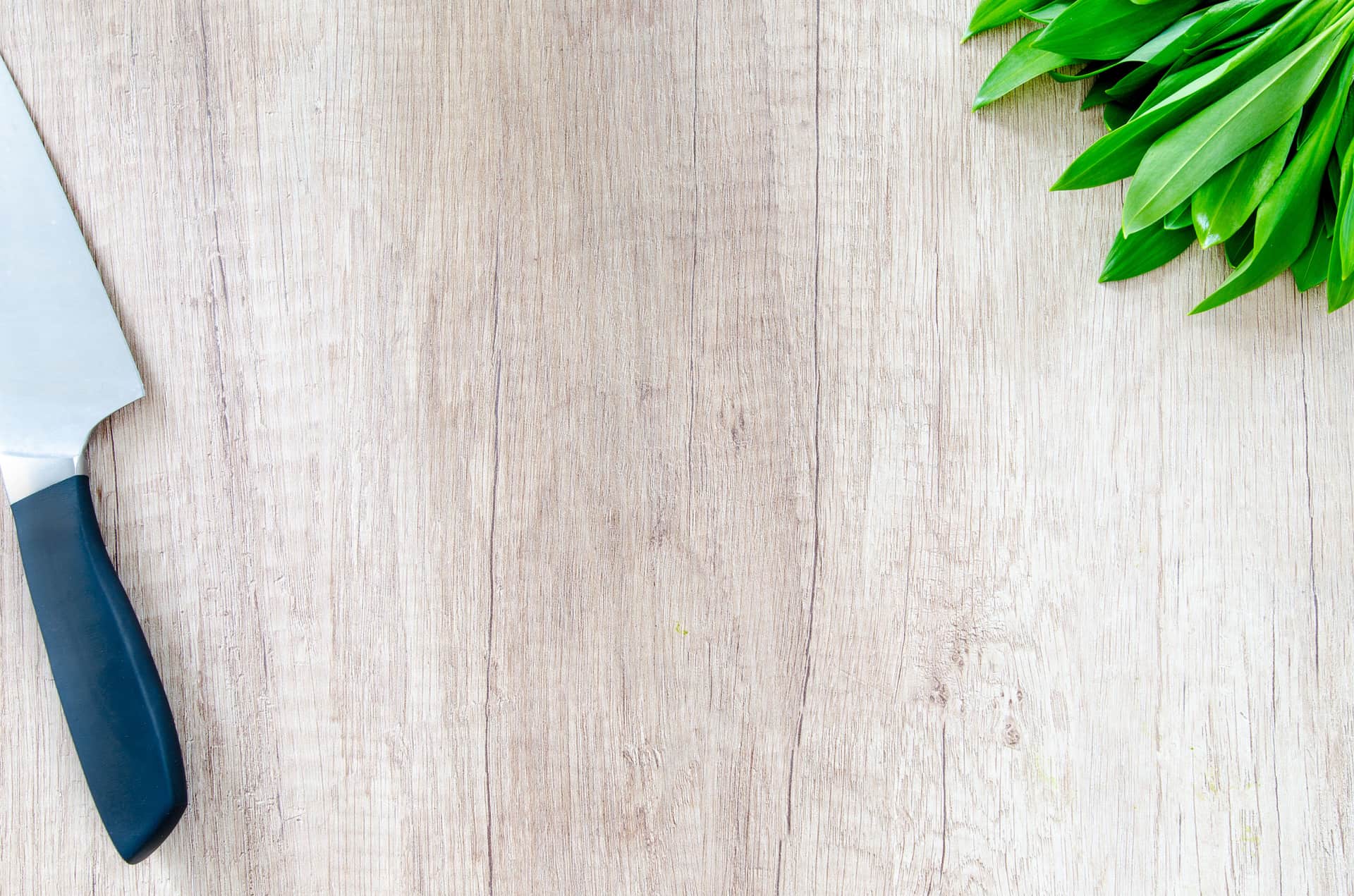 A chef's knife resting on a wooden workbench in natural daylight